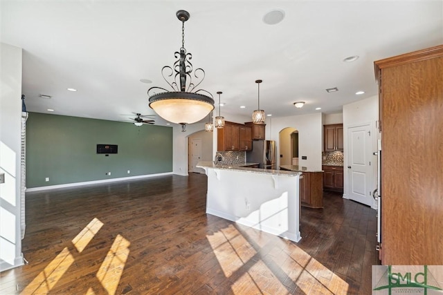 kitchen with arched walkways, a breakfast bar area, open floor plan, freestanding refrigerator, and a peninsula