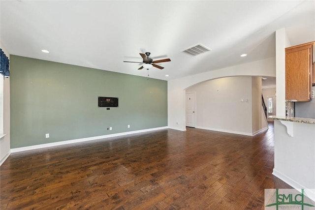 unfurnished living room featuring ceiling fan, arched walkways, dark wood-style flooring, visible vents, and baseboards