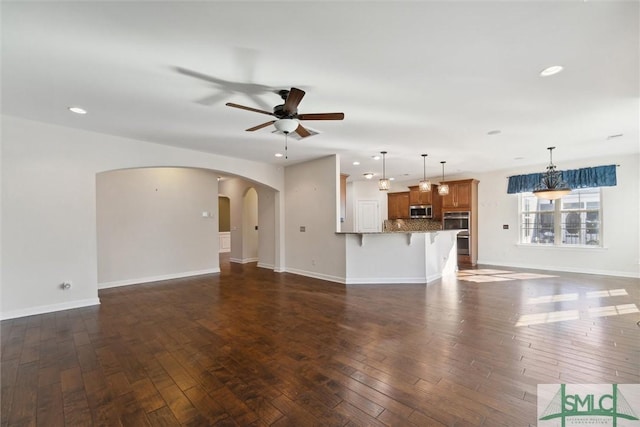 unfurnished living room featuring baseboards, arched walkways, dark wood-style flooring, and a ceiling fan