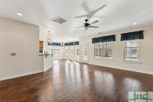 unfurnished living room with ceiling fan, a sink, visible vents, baseboards, and dark wood finished floors