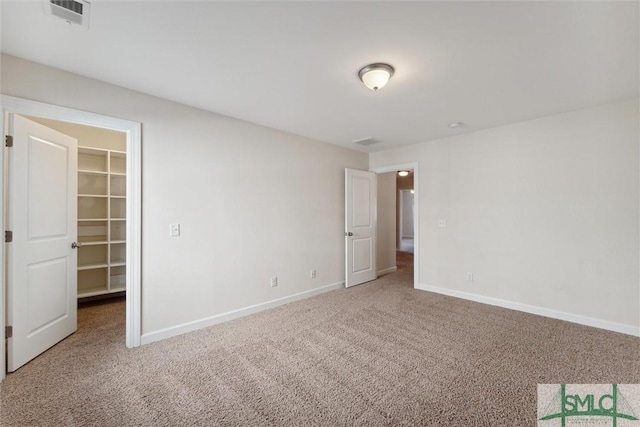 unfurnished bedroom with carpet floors, a walk in closet, visible vents, and baseboards