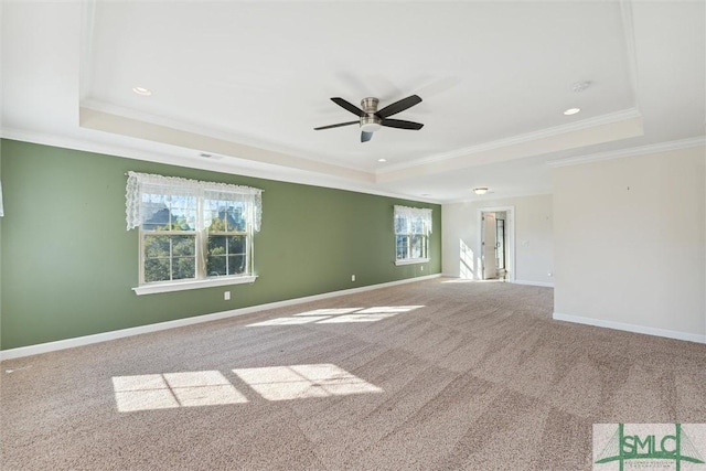 carpeted spare room featuring ornamental molding, a tray ceiling, baseboards, and a ceiling fan