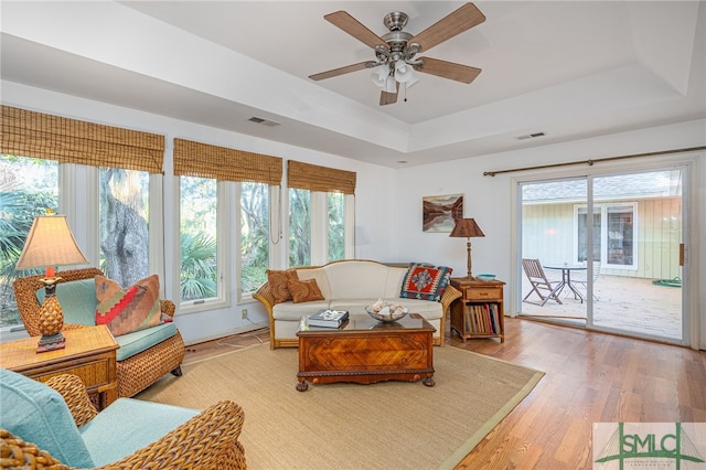 living room with hardwood / wood-style floors, ceiling fan, and a tray ceiling