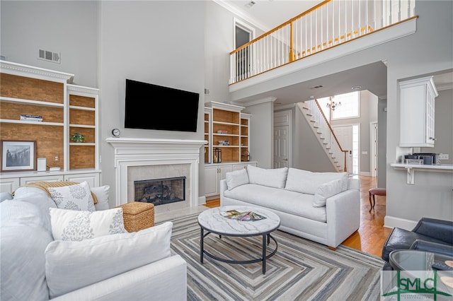 living room featuring a high ceiling, light wood-type flooring, built in shelves, and crown molding