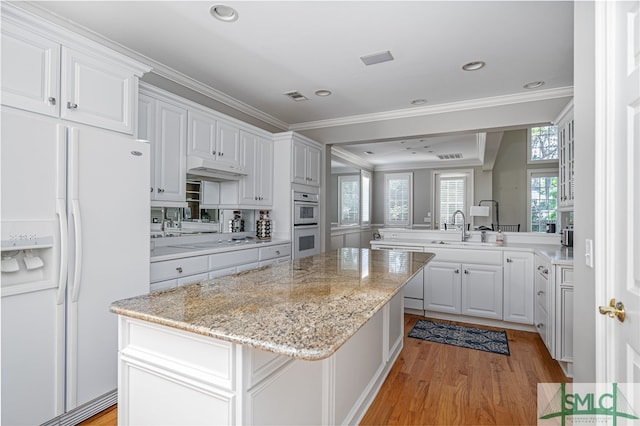 kitchen featuring kitchen peninsula, ornamental molding, white appliances, sink, and white cabinetry