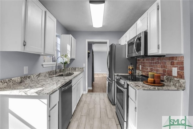 kitchen with stainless steel appliances, light wood-style flooring, decorative backsplash, white cabinets, and a sink