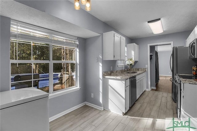 kitchen with sink, stone counters, white cabinetry, appliances with stainless steel finishes, and a textured ceiling