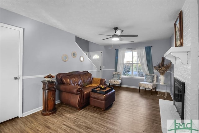 living room with a brick fireplace, a textured ceiling, hardwood / wood-style floors, and ceiling fan