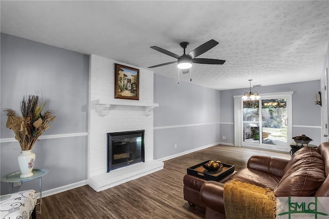 living area with baseboards, wood finished floors, a textured ceiling, a fireplace, and ceiling fan with notable chandelier