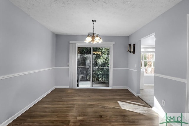 unfurnished dining area featuring an inviting chandelier, a textured ceiling, baseboards, and wood finished floors