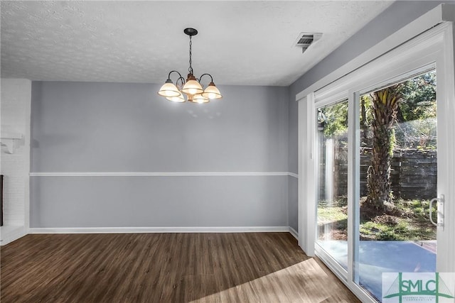 unfurnished dining area with a notable chandelier, visible vents, a textured ceiling, wood finished floors, and baseboards