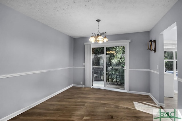 unfurnished dining area with a chandelier, a wealth of natural light, baseboards, and wood finished floors