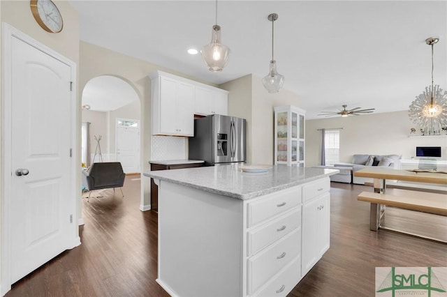 kitchen with dark hardwood / wood-style floors, stainless steel fridge, a kitchen island, light stone counters, and white cabinetry