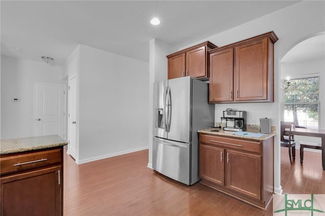 kitchen featuring stainless steel fridge with ice dispenser, light wood-type flooring, and light stone counters