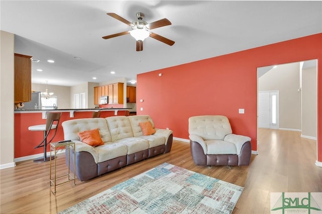 living room with ceiling fan with notable chandelier and light hardwood / wood-style flooring