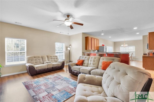 living room featuring ceiling fan with notable chandelier and light hardwood / wood-style floors