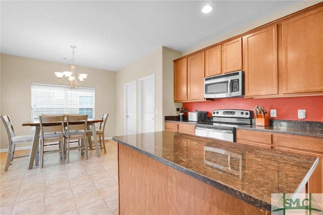 kitchen featuring appliances with stainless steel finishes, dark stone counters, decorative light fixtures, a chandelier, and a kitchen island