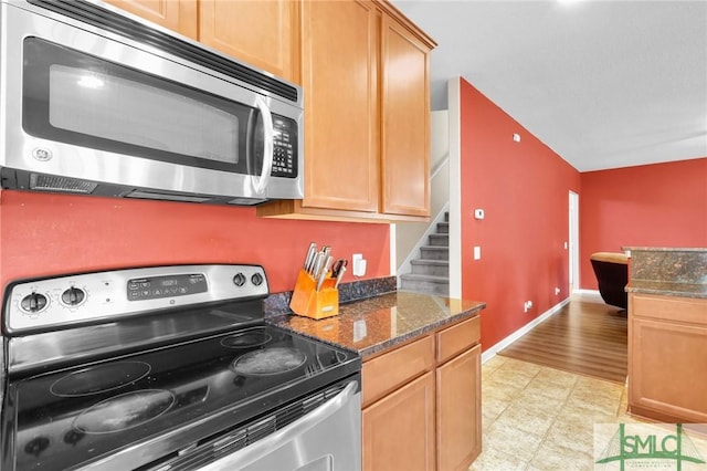 kitchen featuring vaulted ceiling, light hardwood / wood-style flooring, appliances with stainless steel finishes, and dark stone counters