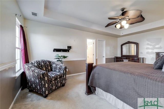 carpeted bedroom with a raised ceiling and ceiling fan