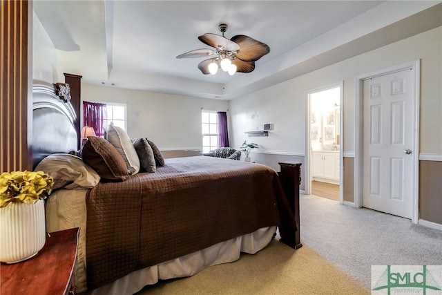 carpeted bedroom featuring ceiling fan, a raised ceiling, and connected bathroom