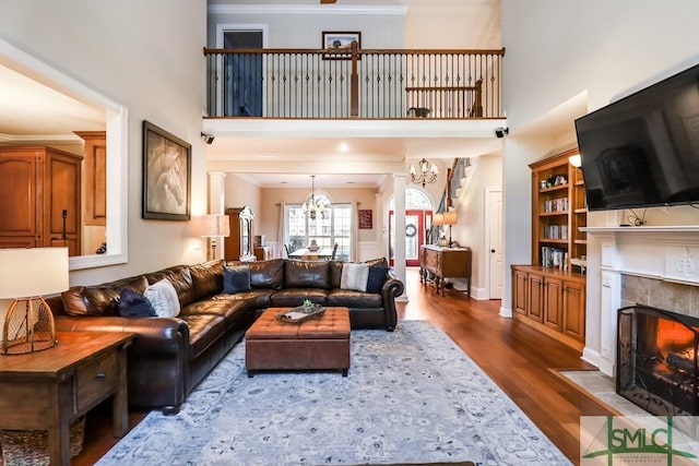 living room featuring a towering ceiling, a tiled fireplace, crown molding, dark wood-type flooring, and an inviting chandelier