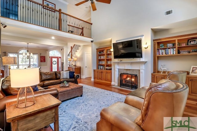 living room with a high ceiling, a tile fireplace, ceiling fan with notable chandelier, and light hardwood / wood-style flooring