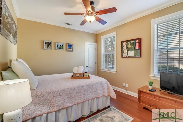 bedroom with multiple windows, hardwood / wood-style floors, ornamental molding, and ceiling fan