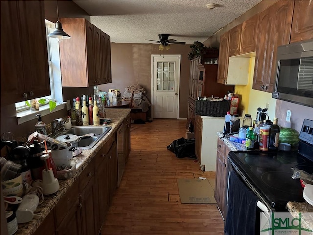 kitchen featuring appliances with stainless steel finishes, hanging light fixtures, a textured ceiling, light hardwood / wood-style flooring, and sink