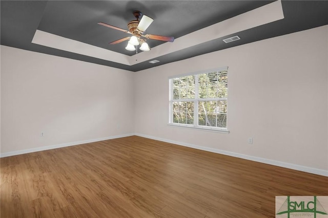 empty room with hardwood / wood-style floors, a tray ceiling, and ceiling fan