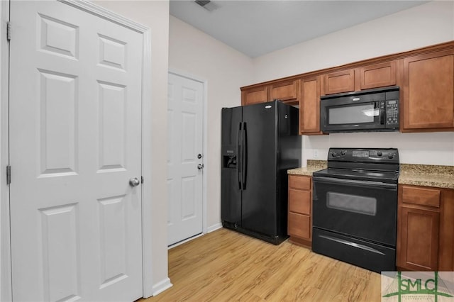 kitchen featuring light stone countertops, light hardwood / wood-style floors, and black appliances