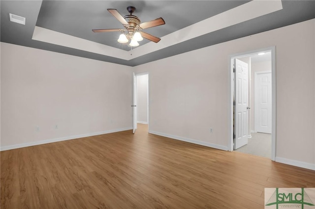 spare room with wood-type flooring, a raised ceiling, and ceiling fan