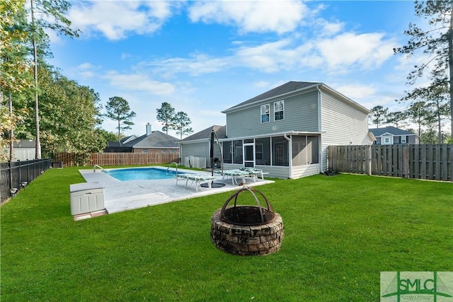 rear view of property with a sunroom, a yard, an outdoor fire pit, a fenced in pool, and a patio area