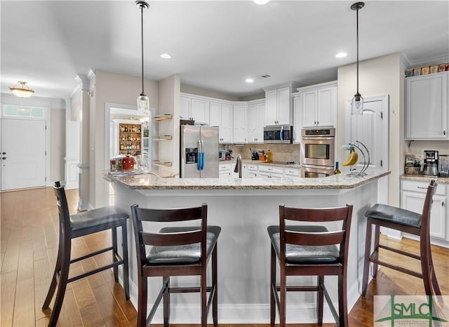 kitchen with appliances with stainless steel finishes, a large island with sink, decorative light fixtures, dark hardwood / wood-style floors, and white cabinetry