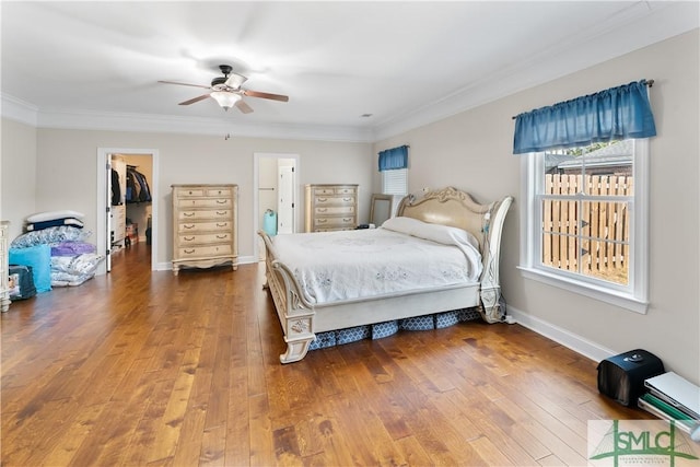 bedroom with ceiling fan, a spacious closet, ornamental molding, wood-type flooring, and a closet