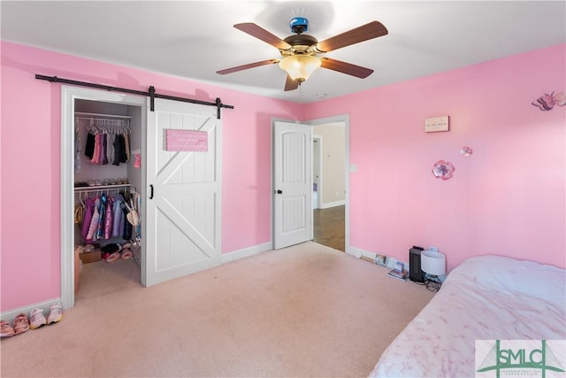 bedroom featuring ceiling fan, a barn door, light carpet, and a closet