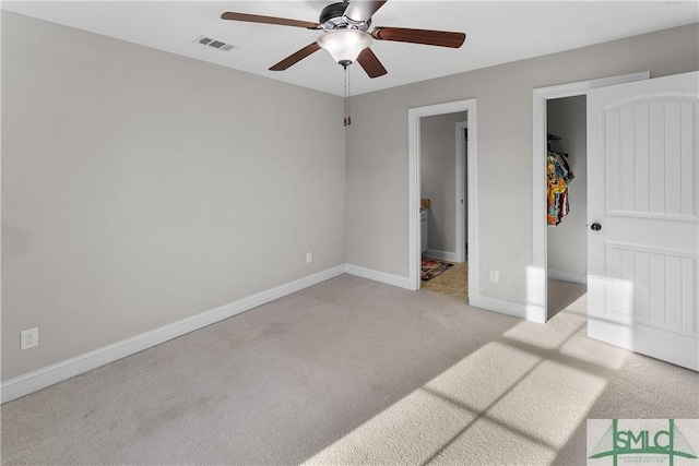 unfurnished bedroom featuring light carpet, a closet, a spacious closet, and ceiling fan