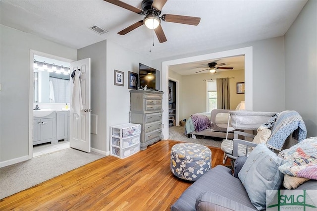 bedroom with light wood-type flooring, ensuite bath, ceiling fan, and sink