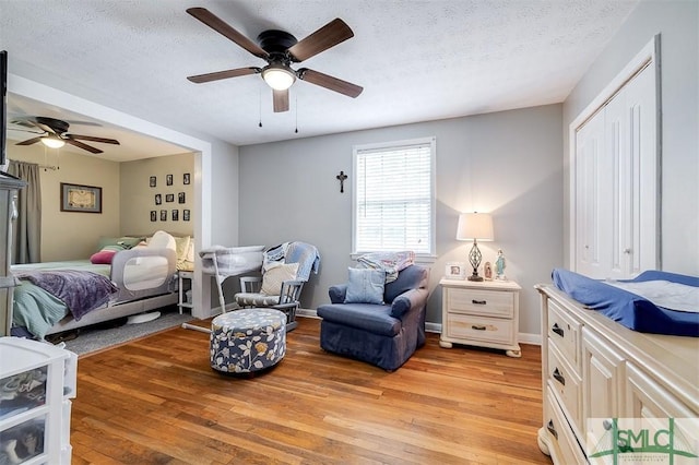 bedroom with ceiling fan, light wood-type flooring, and a textured ceiling