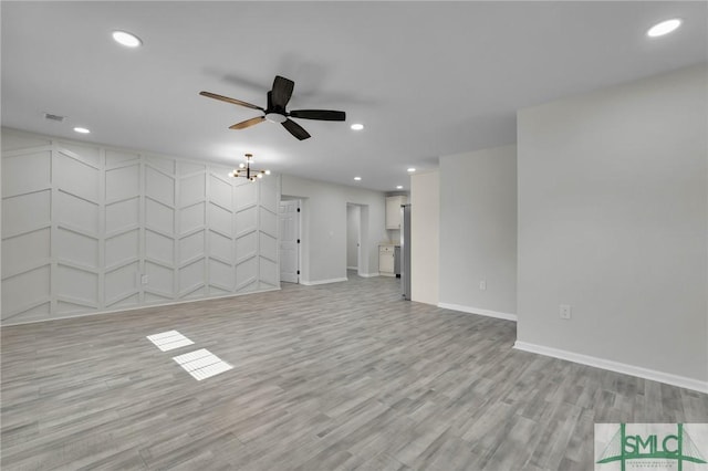 unfurnished living room with ceiling fan with notable chandelier and light hardwood / wood-style floors