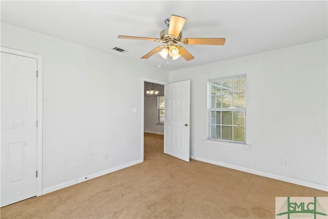 carpeted spare room featuring ceiling fan with notable chandelier