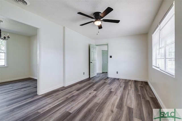 empty room with a textured ceiling, dark hardwood / wood-style floors, and a healthy amount of sunlight