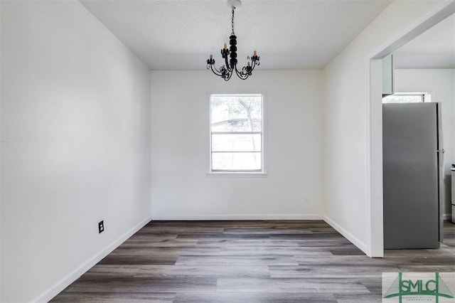 unfurnished dining area with dark hardwood / wood-style floors, a textured ceiling, and an inviting chandelier