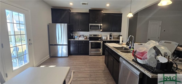 kitchen featuring sink, stainless steel appliances, light stone counters, pendant lighting, and light hardwood / wood-style floors