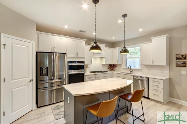 kitchen with hanging light fixtures, a kitchen island, appliances with stainless steel finishes, white cabinets, and light wood-type flooring