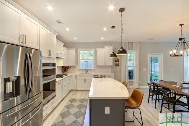 kitchen with a center island, white cabinets, sink, decorative light fixtures, and stainless steel appliances