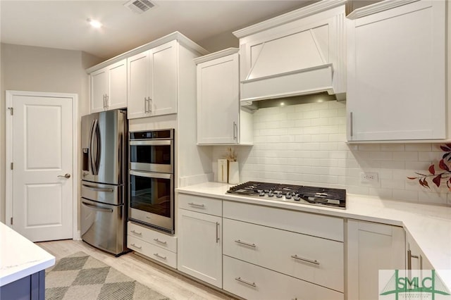 kitchen with tasteful backsplash, light hardwood / wood-style flooring, white cabinets, and appliances with stainless steel finishes