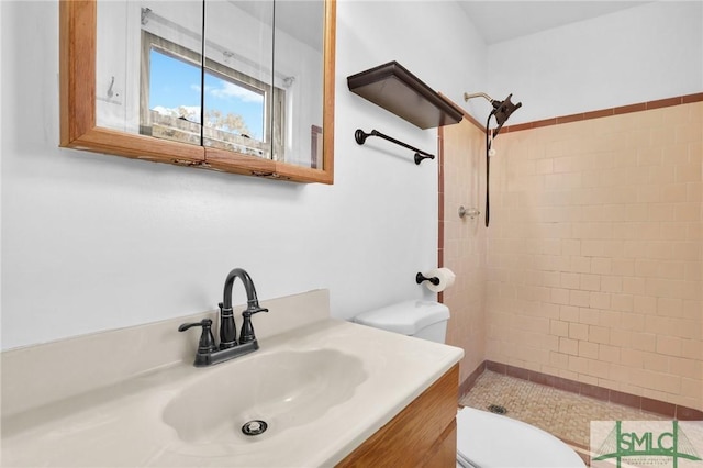 bathroom featuring a tile shower, vanity, and toilet