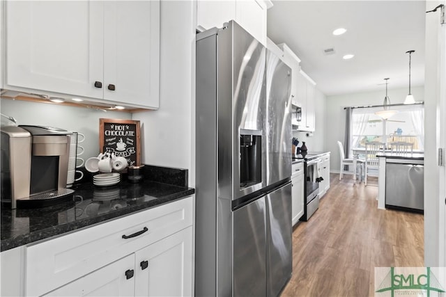 kitchen with white cabinetry, hanging light fixtures, light hardwood / wood-style flooring, dark stone counters, and appliances with stainless steel finishes