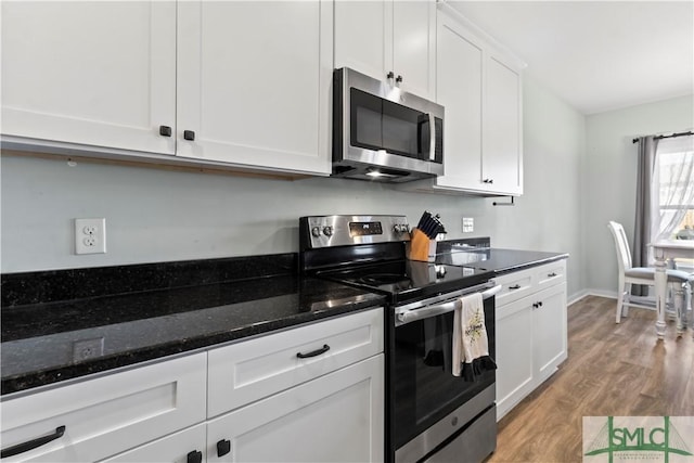 kitchen with white cabinets, dark stone countertops, stainless steel appliances, and light hardwood / wood-style flooring