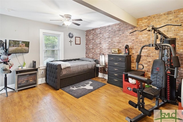 bedroom featuring beamed ceiling, wood-type flooring, ceiling fan, and brick wall